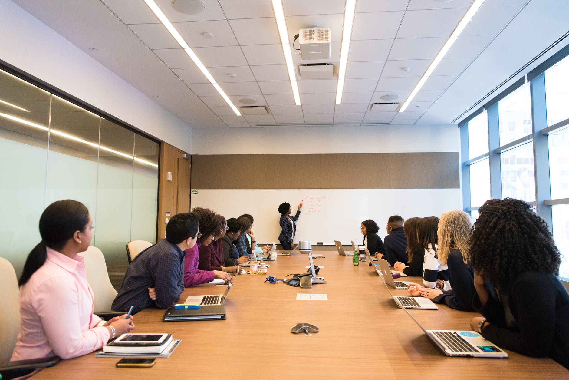 Image of a team around a worktable looking at a presenter at the front of the room writing on a board.
Photo by Christina Morillo on Pexels.com
